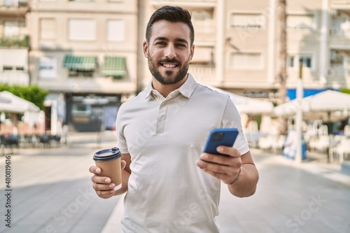 Young hispanic man using smartphone drinking coffee at street © Krakenimages.com