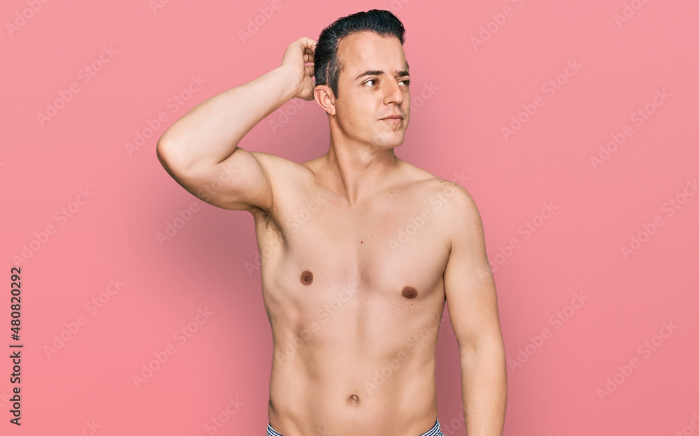 Handsome young man wearing swimwear shirtless confuse and wondering about question. uncertain with doubt, thinking with hand on head. pensive concept.