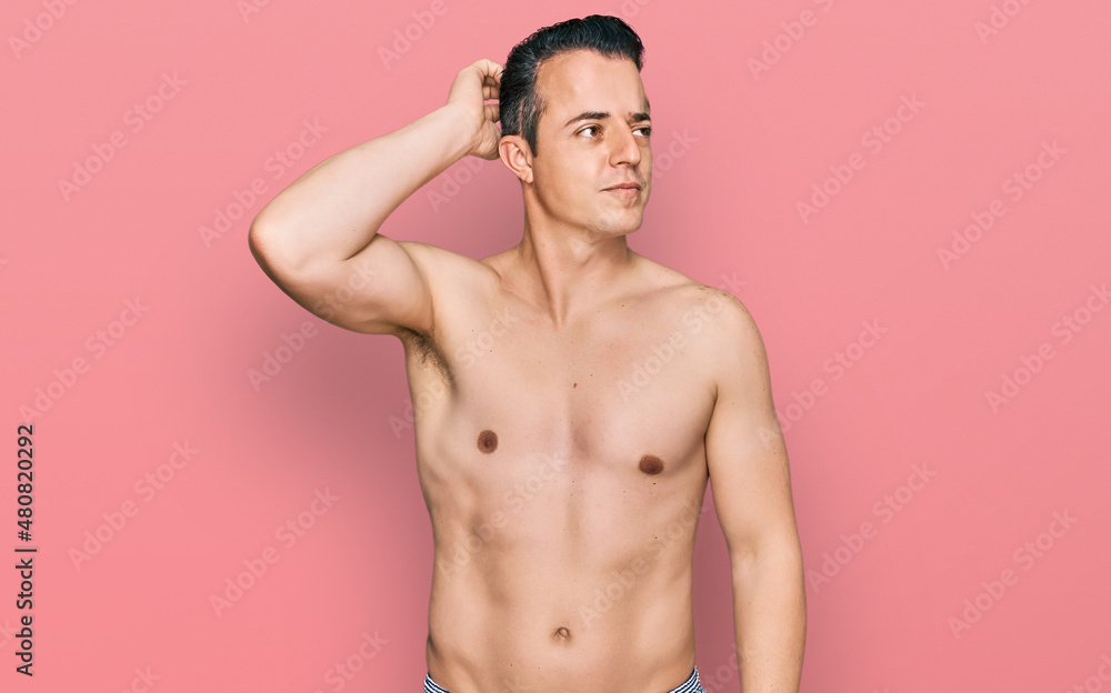 Fototapeta premium Handsome young man wearing swimwear shirtless confuse and wondering about question. uncertain with doubt, thinking with hand on head. pensive concept.