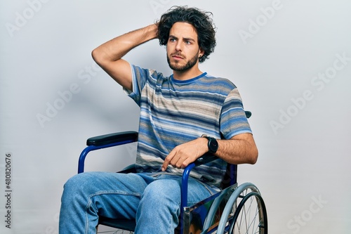 Handsome hispanic man sitting on wheelchair confuse and wondering about question. uncertain with doubt, thinking with hand on head. pensive concept.