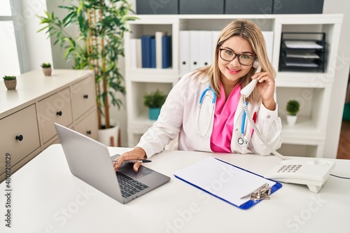 Young hispanic woman wearing doctor uniform talking on the telephone working al clinic