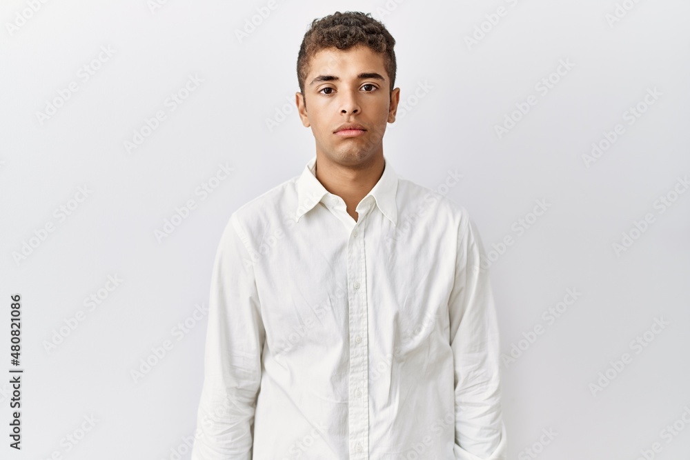 Young handsome hispanic man standing over isolated background relaxed with serious expression on face. simple and natural looking at the camera. Young handsome hispanic man standing over isolated background relaxed with serious expression on face. simple and natural looking at the camera.