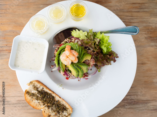 Top view of fresh seafood ceviche with dressing and lettuce on side. Chopped salmon, prawns and avocado slices on white plate. Gourmet restaurant food concept