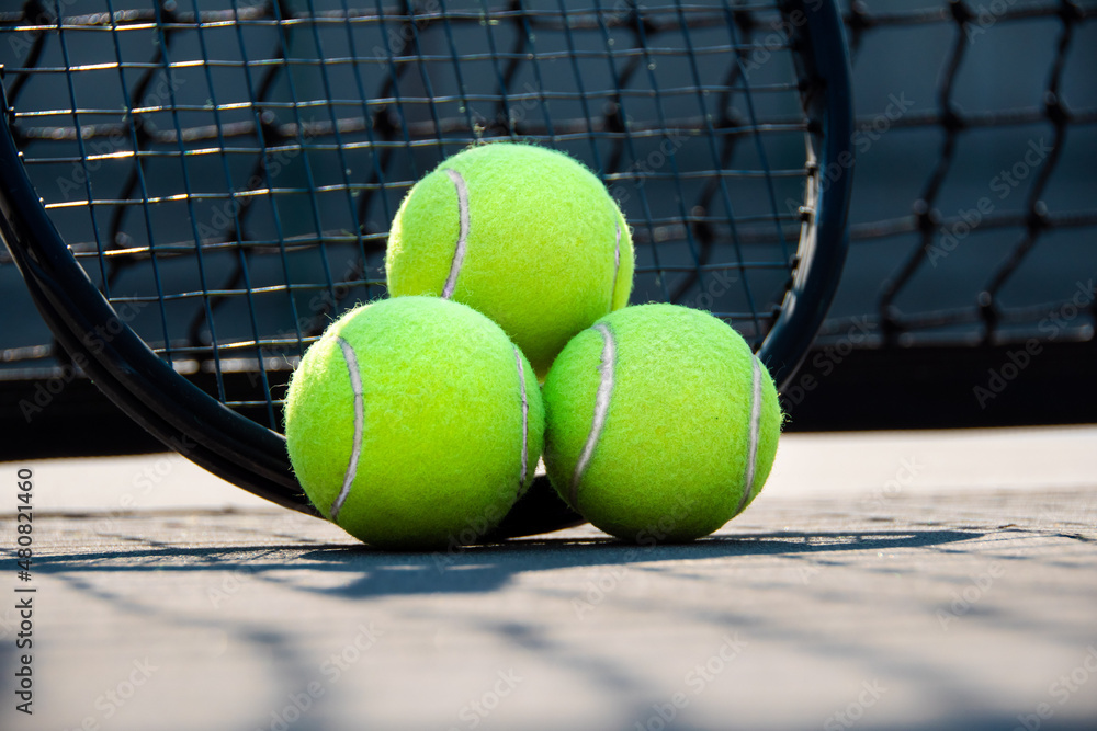 close up of Tennis racket and three balls leaned against the net in hard court
