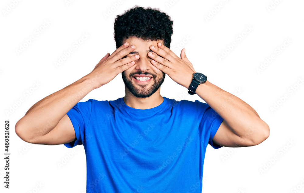 Young arab man with beard wearing casual blue t shirt covering eyes with hands smiling cheerful and funny. blind concept. Young arab man with beard wearing casual blue t shirt covering eyes with hands smiling cheerful and funny. blind concept.