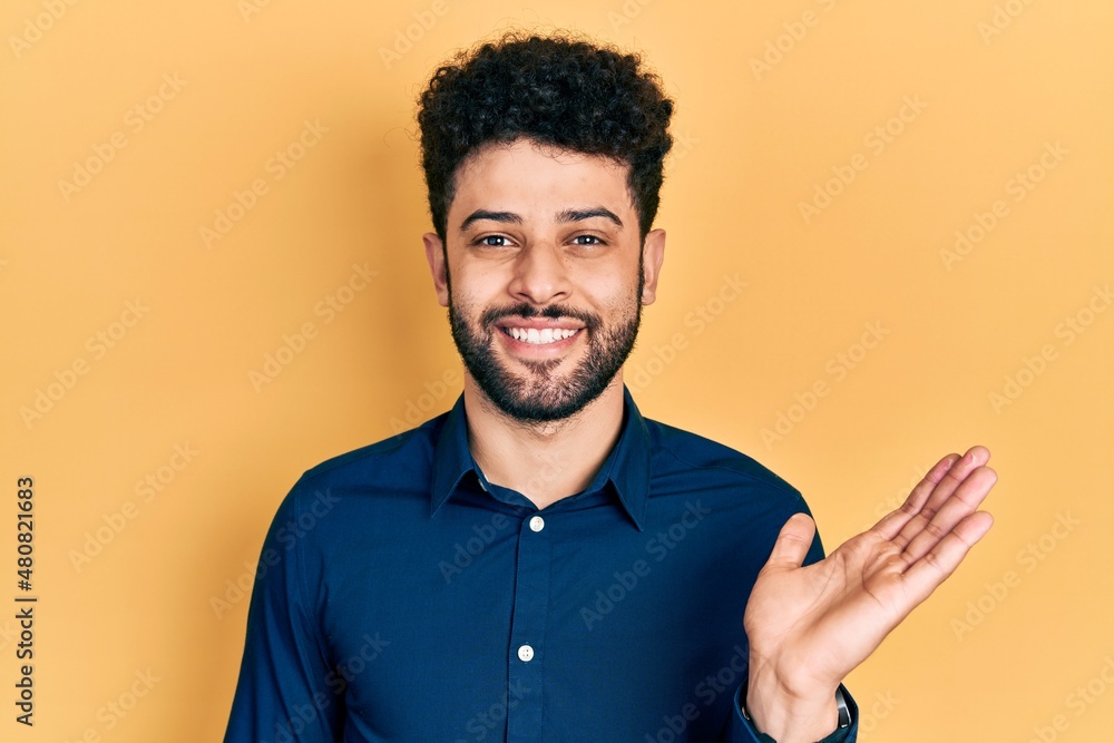Young arab man with beard wearing casual shirt smiling cheerful presenting and pointing with palm of hand looking at the camera. Young arab man with beard wearing casual shirt smiling cheerful presenting and pointing with palm of hand looking at the camera.
