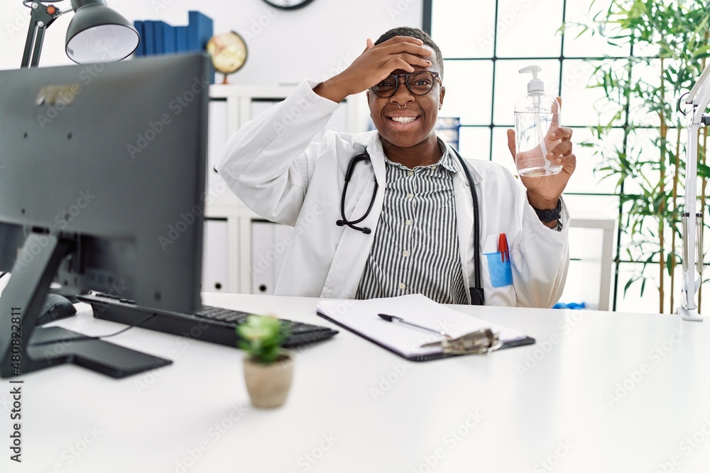 Young african doctor man holding hand sanitizer gel at the clinic stressed and frustrated with hand on head, surprised and angry face Young african doctor man holding hand sanitizer gel at the clinic stressed and frustrated with hand on head, surprised and angry face