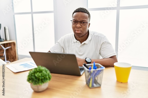 Young african man working at the office using computer laptop looking sleepy and tired, exhausted for fatigue and hangover, lazy eyes in the morning.