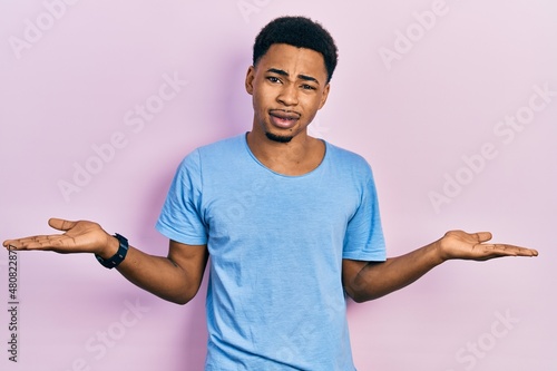 Young african american man wearing casual blue t shirt clueless and confused with open arms, no idea concept. photo