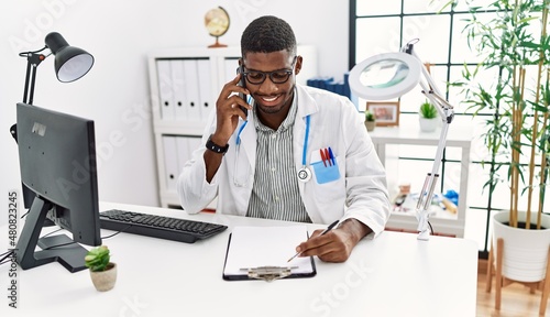Young african american man wearing doctor uniform talking on the smartphone at clinic