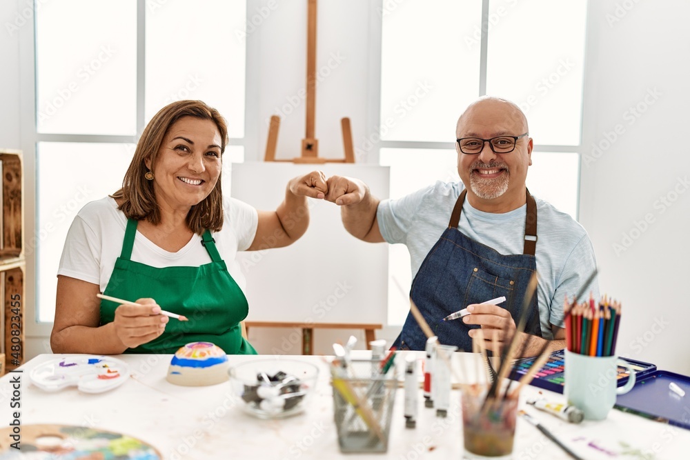 Middle age hispanic painter couple smiling happy bump fists at art studio. Middle age hispanic painter couple smiling happy bump fists at art studio.