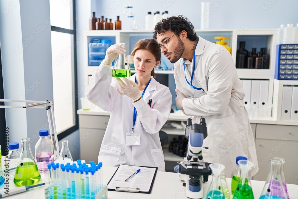 Man and woman scientist partners looking test tube at laboratory Man and woman scientist partners looking test tube at laboratory