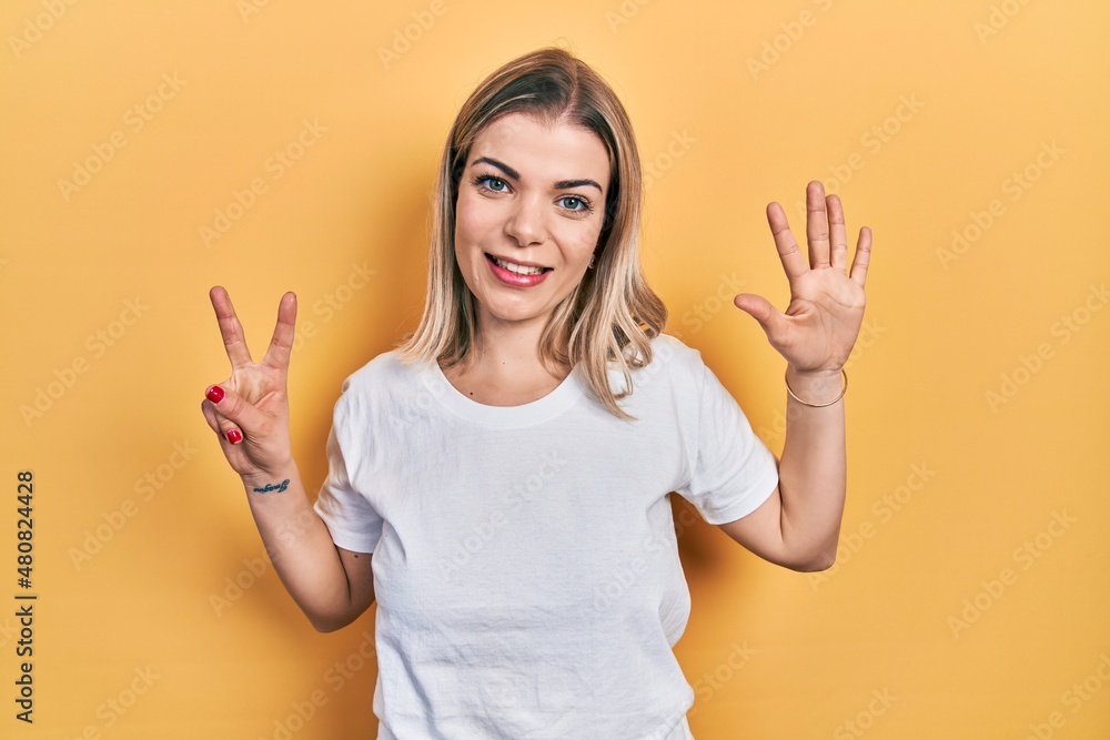 Beautiful caucasian woman wearing casual white t shirt showing and pointing up with fingers number seven while smiling confident and happy.