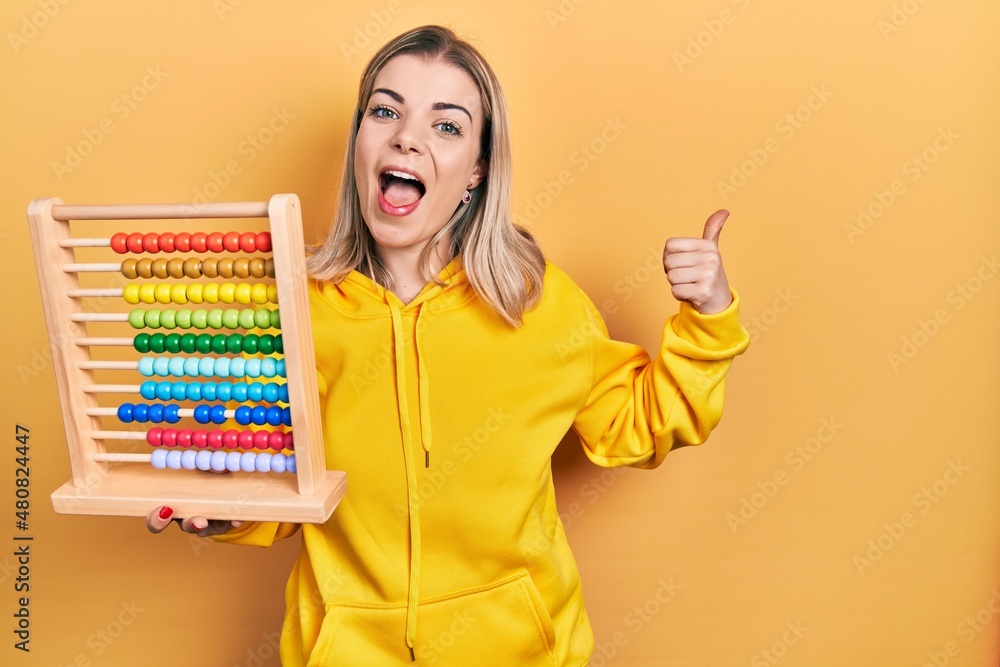 Beautiful caucasian woman holding traditional abacus pointing thumb up to the side smiling happy with open mouth Beautiful caucasian woman holding traditional abacus pointing thumb up to the side smiling happy with open mouth