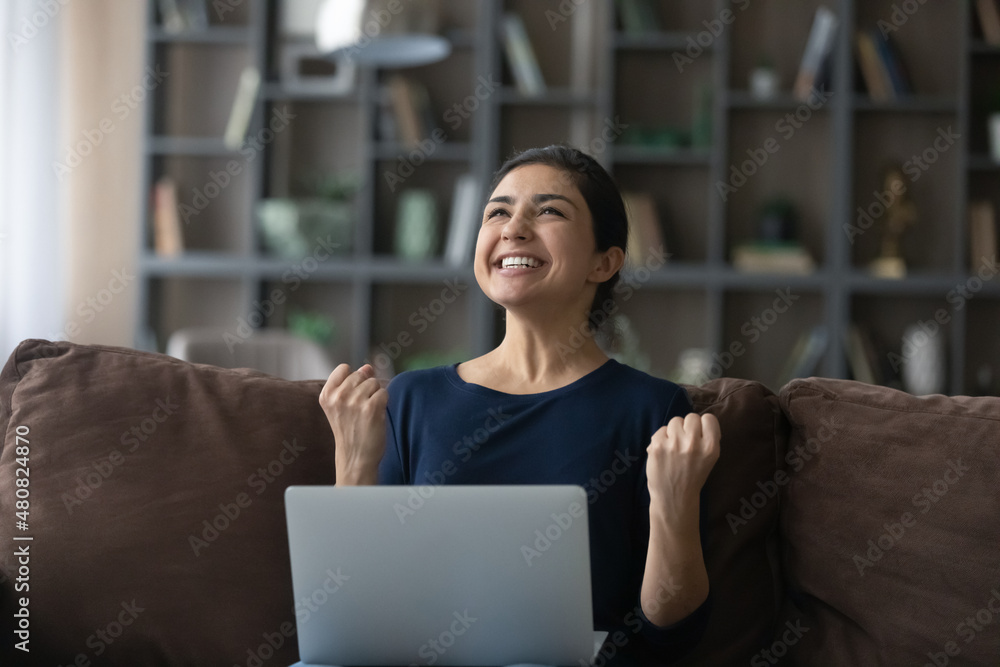 Naklejka premium Overjoyed young Indian woman celebrating getting good news, reading email with unbelievable win news, feeling excited of received dream job offer, online lottery gambling win, internet success concept
