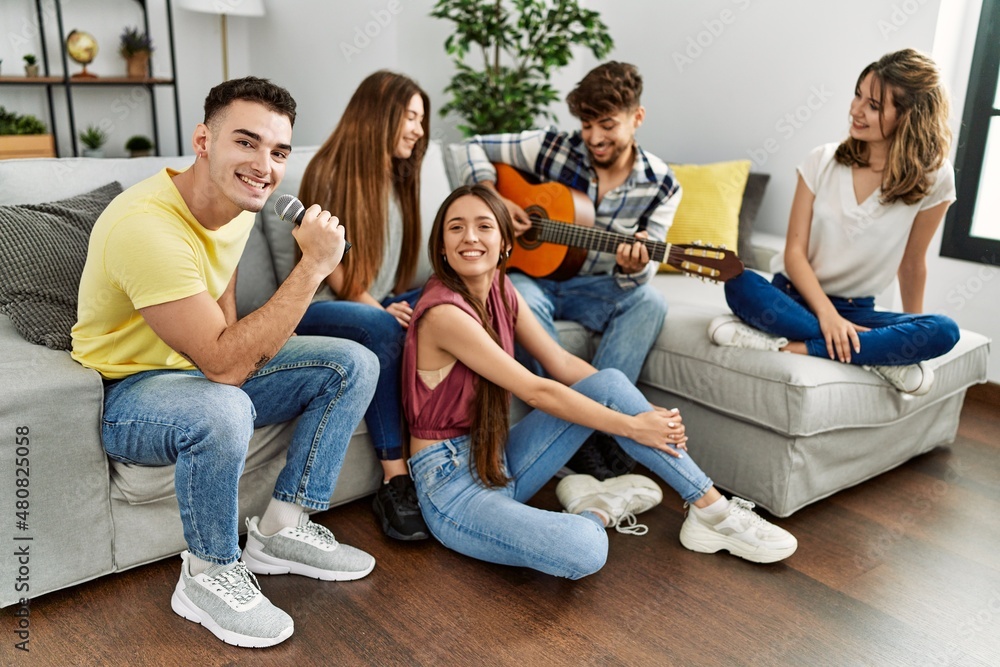 Obraz premium Group of young friends on party playing classical guitar and singing song at home.
