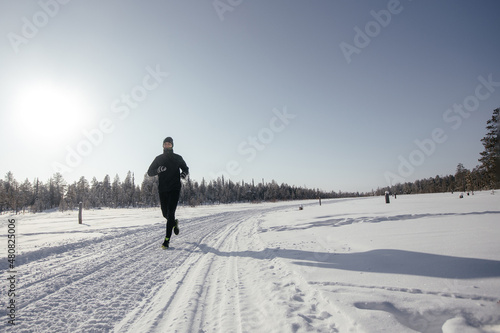 Sporty young man in sportswear jogging through a snowy winter forest. Playing sports in cold weather. The concept of seasonal sports and acclimatization training