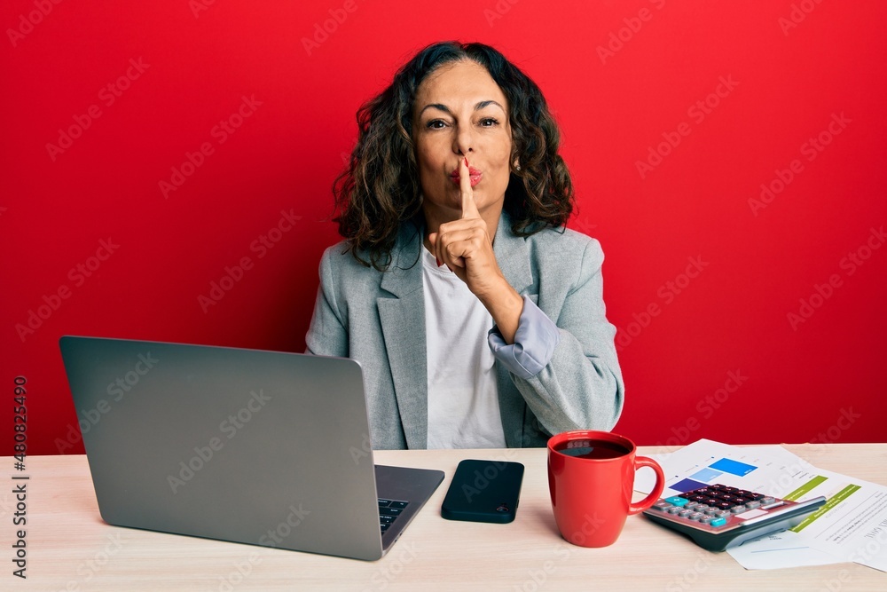 Beautiful middle age woman working at the office drinking a cup of coffee asking to be quiet with finger on lips. silence and secret concept. Beautiful middle age woman working at the office drinking a cup of coffee asking to be quiet with finger on lips. silence and secret concept.