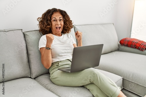 Middle age hispanic woman working using computer laptop at home screaming proud, celebrating victory and success very excited with raised arms