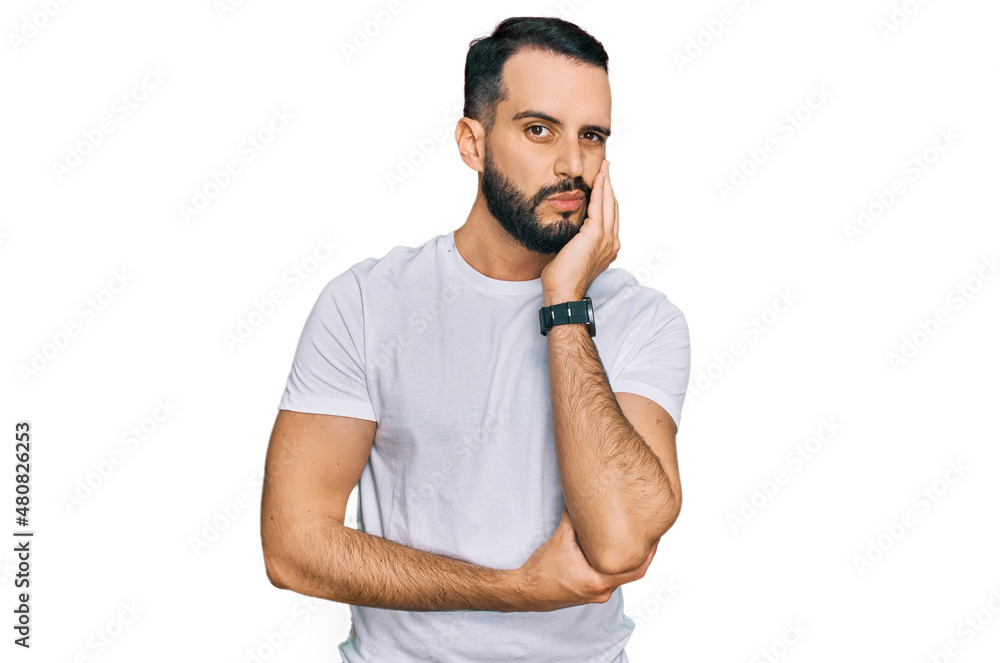 Young man with beard wearing casual white t shirt thinking looking tired and bored with depression problems with crossed arms. Young man with beard wearing casual white t shirt thinking looking tired and bored with depression problems with crossed arms.