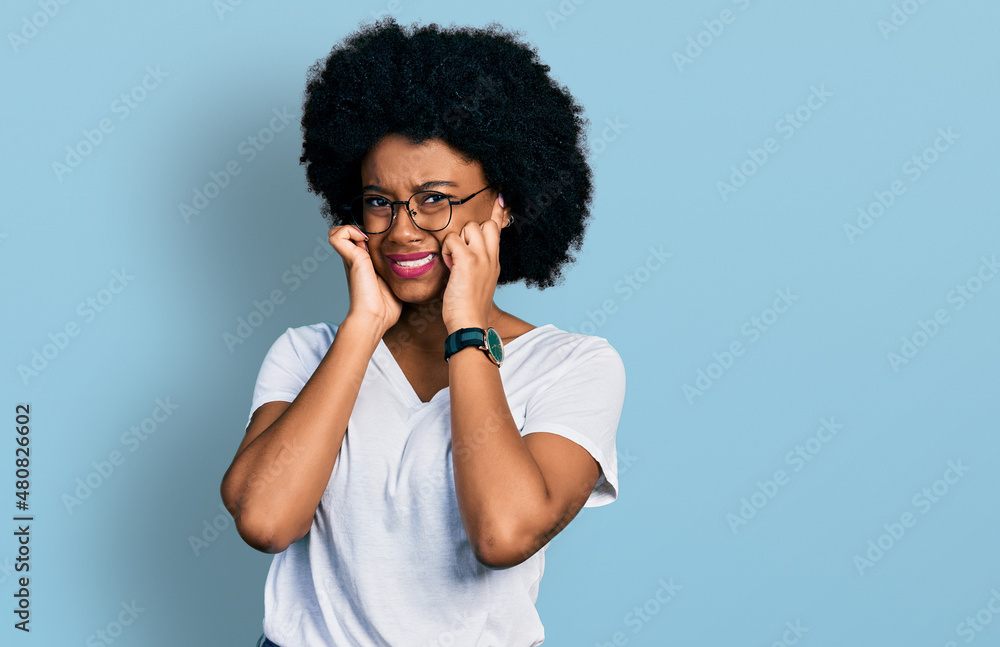 Young african american woman wearing casual white t shirt covering ears with fingers with annoyed expression for the noise of loud music. deaf concept. Young african american woman wearing casual white t shirt covering ears with fingers with annoyed expression for the noise of loud music. deaf concept.
