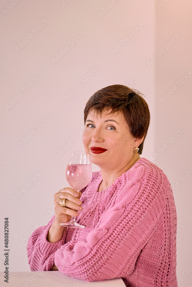 cheerful Mature woman in pink sweater drinking rose wine and smiling. self-sufficiency, holiday, celebrate concept cheerful Mature woman in pink sweater drinking rose wine and smiling. self-sufficiency, holiday, celebrate concept