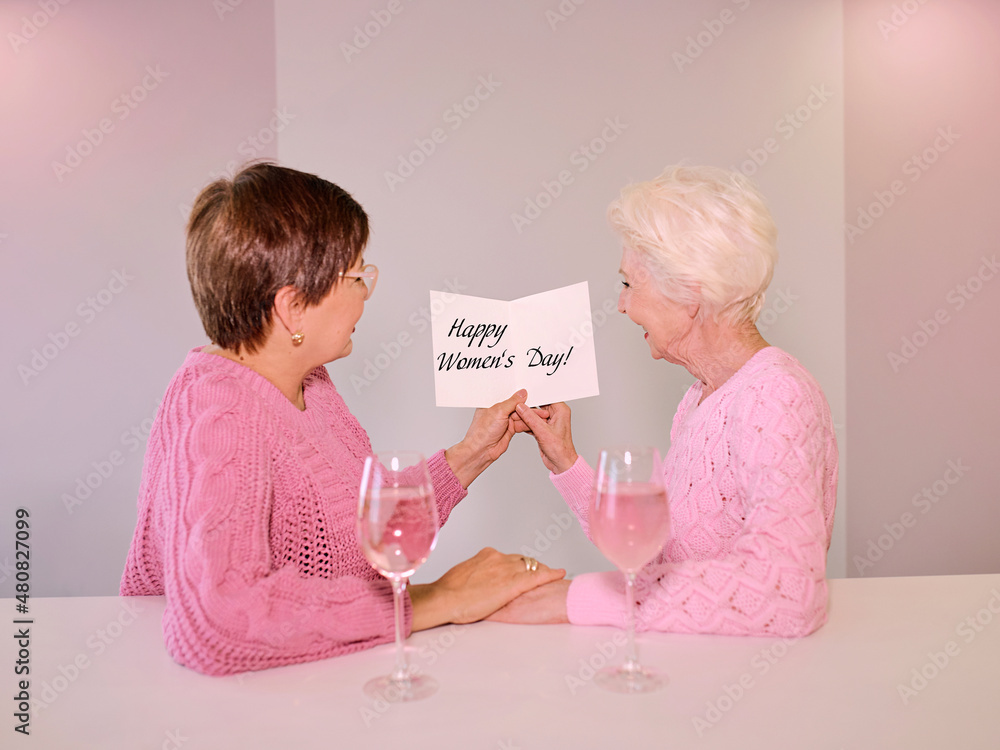 Two mature women drinking wine and giving a post card image