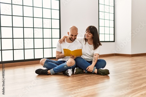 Young hispanic couple smiling happy reading book at empty new home.