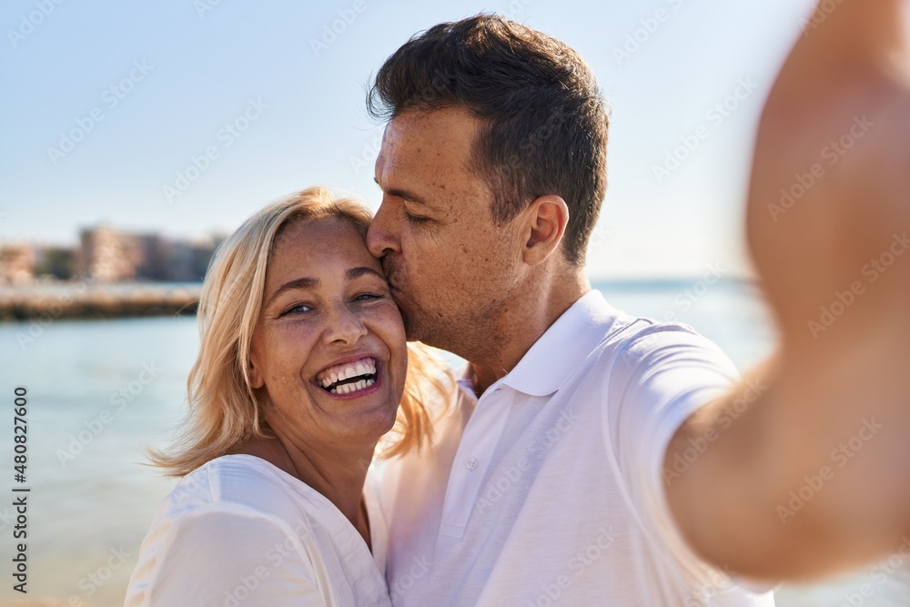 Middle age man and woman couple hugging each other and kissing make selfie by the smartphone at seaside Middle age man and woman couple hugging each other and kissing make selfie by the smartphone at seaside