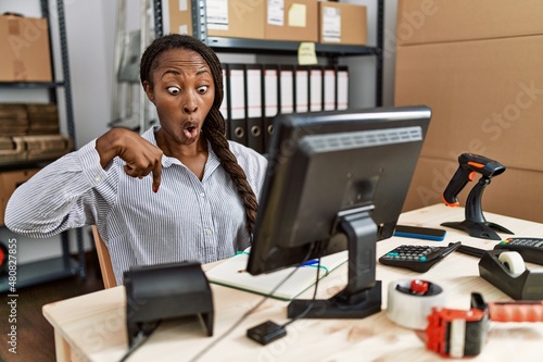 African woman working at small business ecommerce pointing down with fingers showing advertisement, surprised face and open mouth