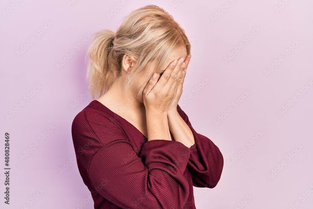 Young blonde woman wearing casual winter sweater with sad expression covering face with hands while crying. depression concept. Young blonde woman wearing casual winter sweater with sad expression covering face with hands while crying. depression concept.