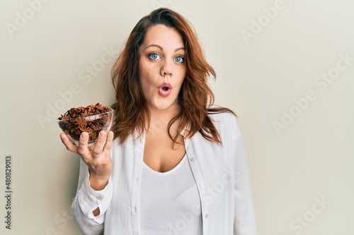 Young caucasian woman holding bowl of star anise scared and amazed with open mouth for surprise  disbelief face