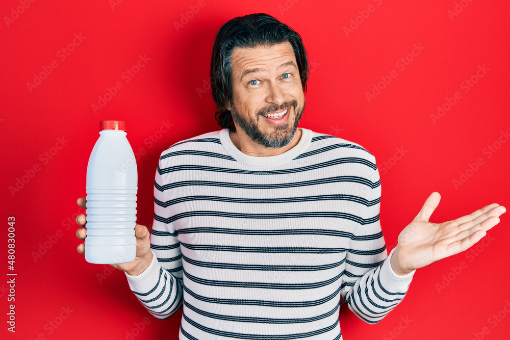 Middle age caucasian man holding liter bottle of milk celebrating achievement with happy smile and winner expression with raised hand Middle age caucasian man holding liter bottle of milk celebrating achievement with happy smile and winner expression with raised hand