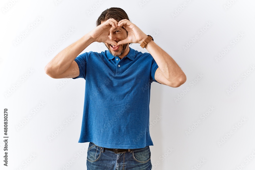 Fototapeta premium Handsome middle age man standing together over isolated background doing heart shape with hand and fingers smiling looking through sign
