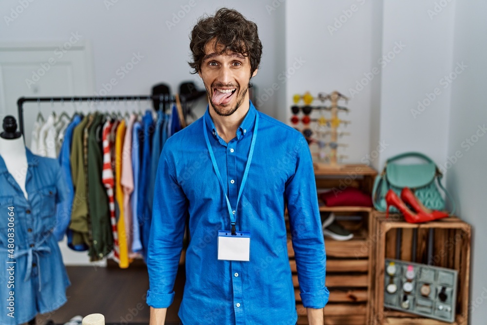 Young hispanic man working as manager at retail boutique sticking tongue out happy with funny expression. emotion concept. Young hispanic man working as manager at retail boutique sticking tongue out happy with funny expression. emotion concept.