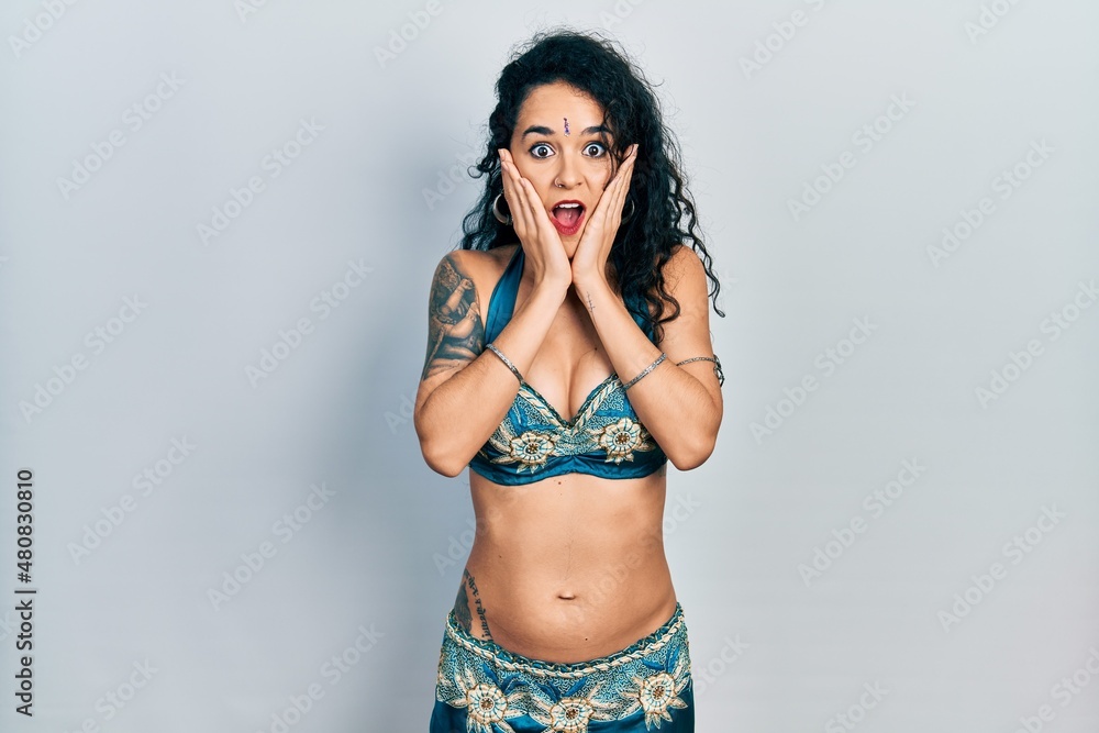 Young woman wearing bindi and traditional belly dance clothes afraid and shocked, surprise and amazed expression with hands on face Young woman wearing bindi and traditional belly dance clothes afraid and shocked, surprise and amazed expression with hands on face