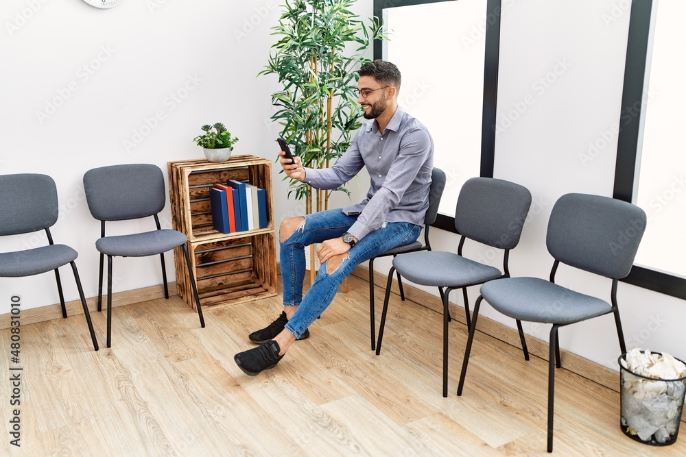 Young arab man using smartphone sitting on chair at waiting room