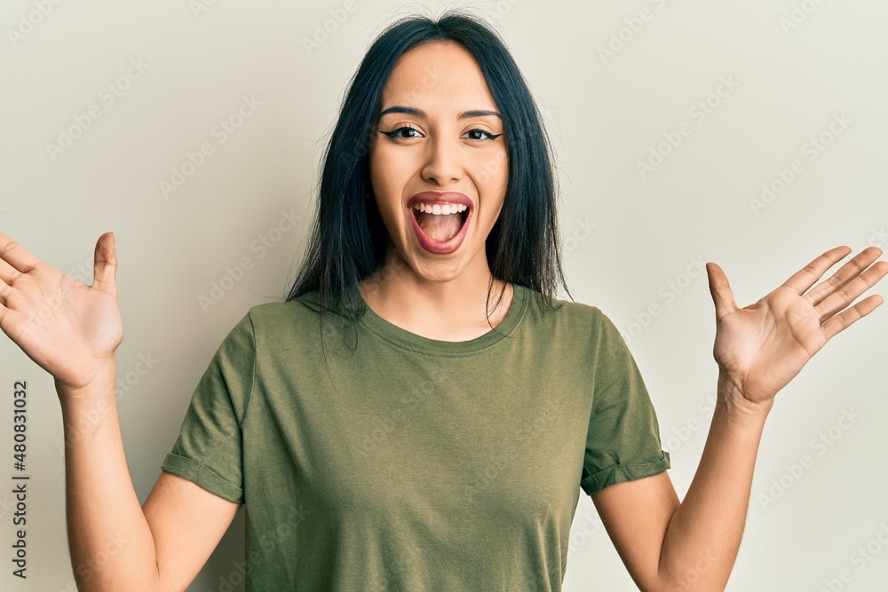 Young hispanic girl wearing casual t shirt celebrating crazy and amazed for success with arms raised and open eyes screaming excited. winner concept Young hispanic girl wearing casual t shirt celebrating crazy and amazed for success with arms raised and open eyes screaming excited. winner concept