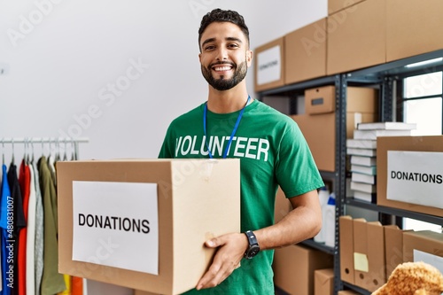 Fotografía Young arab man wearing volunteer uniform holding donations box at charity center