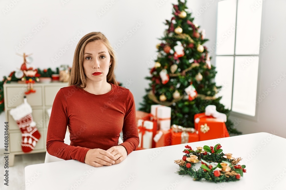 Caucasian young blonde woman sitting on the table by christmas tree depressed and worry for distress, crying angry and afraid. sad expression. Caucasian young blonde woman sitting on the table by christmas tree depressed and worry for distress, crying angry and afraid. sad expression.