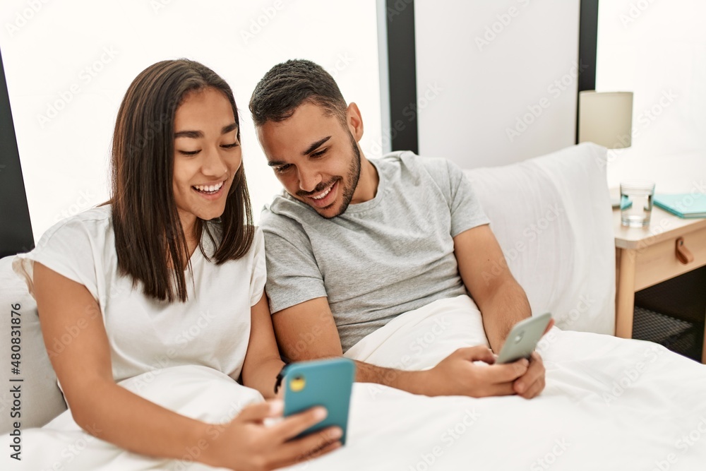 Young latin couple using smartphone lying on bed at home. Young latin couple using smartphone lying on bed at home.