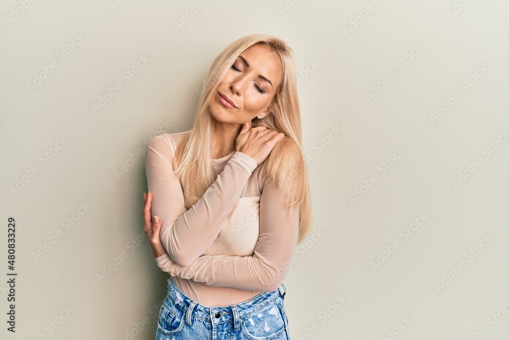 Young blonde woman wearing casual clothes hugging oneself happy and positive, smiling confident. self love and self care Young blonde woman wearing casual clothes hugging oneself happy and positive, smiling confident. self love and self care