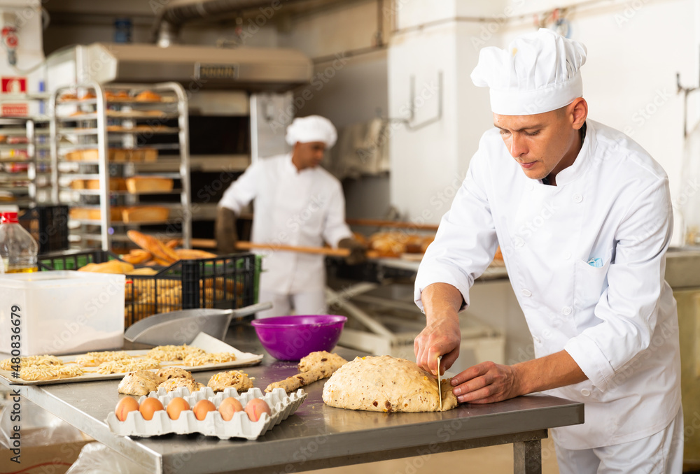 man in chefs uniform kneading dough in bakery