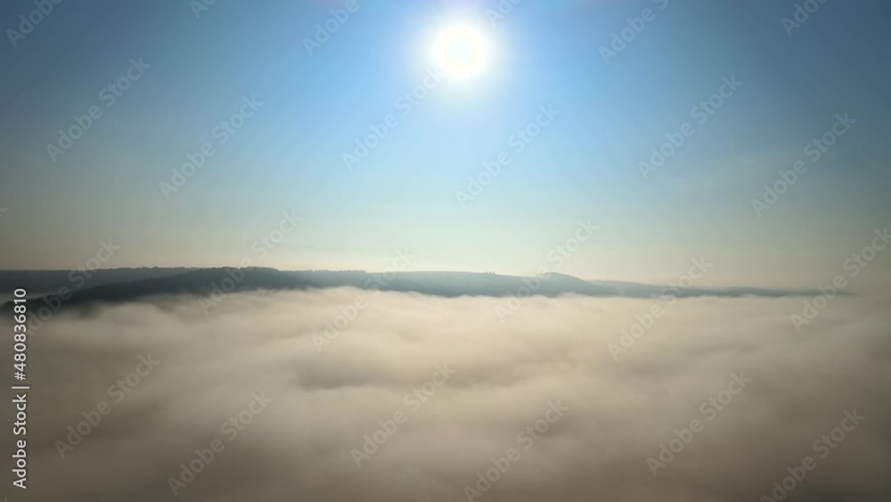 Aerial view of colorful sunrise over white dense fog with distant dark silhouettes of mountain hills on horizon Aerial view of colorful sunrise over white dense fog with distant dark silhouettes of mountain hills on horizon