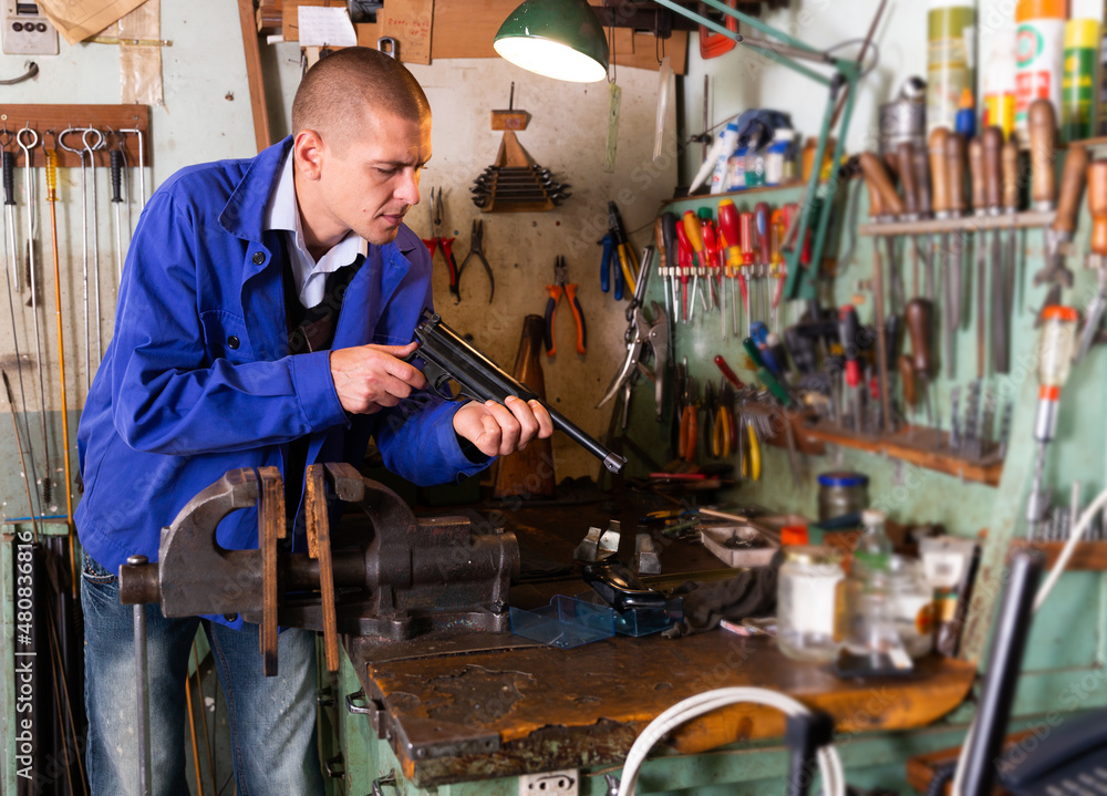 Fototapeta premium Portrait of concentrated skilled craftsman of weapons workshop engaged in repairing of small-bore handgun.
