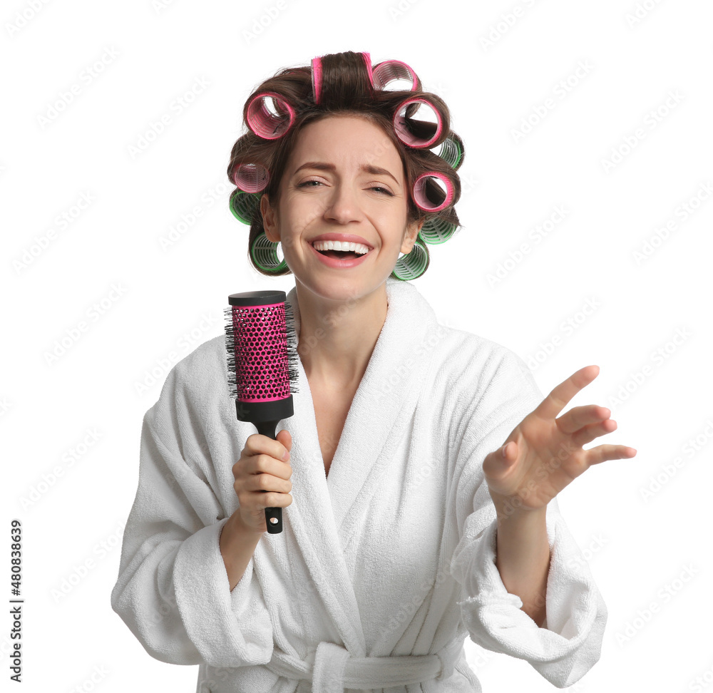 Beautiful young woman in bathrobe with hair curlers singing into hairbrush on white background Beautiful young woman in bathrobe with hair curlers singing into hairbrush on white background