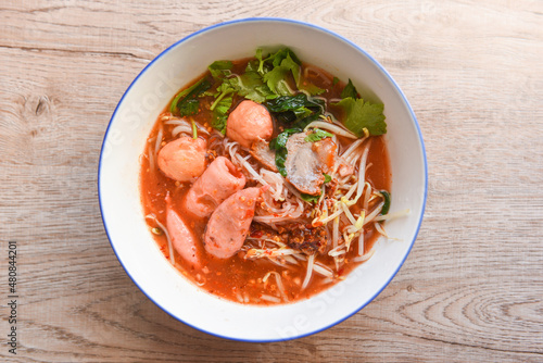 Red soup noodle pork with red roasted pork and bean sprout vegetable in soup bowl on wooden table, top view Thai and China Asian food