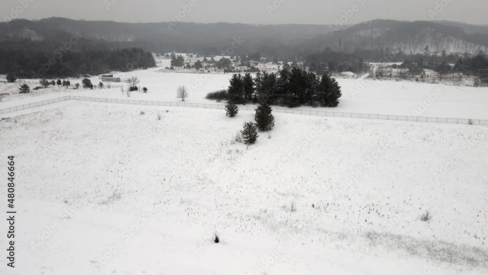 Snowy day in rural valley. Cloudy gray sky. Fields covered with snow. Fence dividing the land. Small grouping of trees. Snowy day in rural valley. Cloudy gray sky. Fields covered with snow. Fence dividing the land. Small grouping of trees.