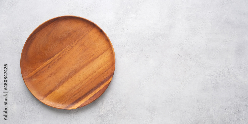 Empty round wooden plate on gray cement table background, banner with