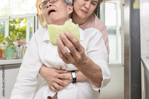 Senior woman with bread stuck in her throat,suffocating due to food clogging the trachea,obstruction of the airway,caregiver doing the heimlich maneuver,helping elderly,choking first aid,life support photo